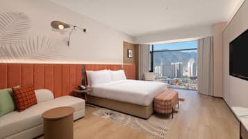 Habitación de hotel moderna con una cama grande, un sofá, una mesita, un televisor y vistas a la ciudad.