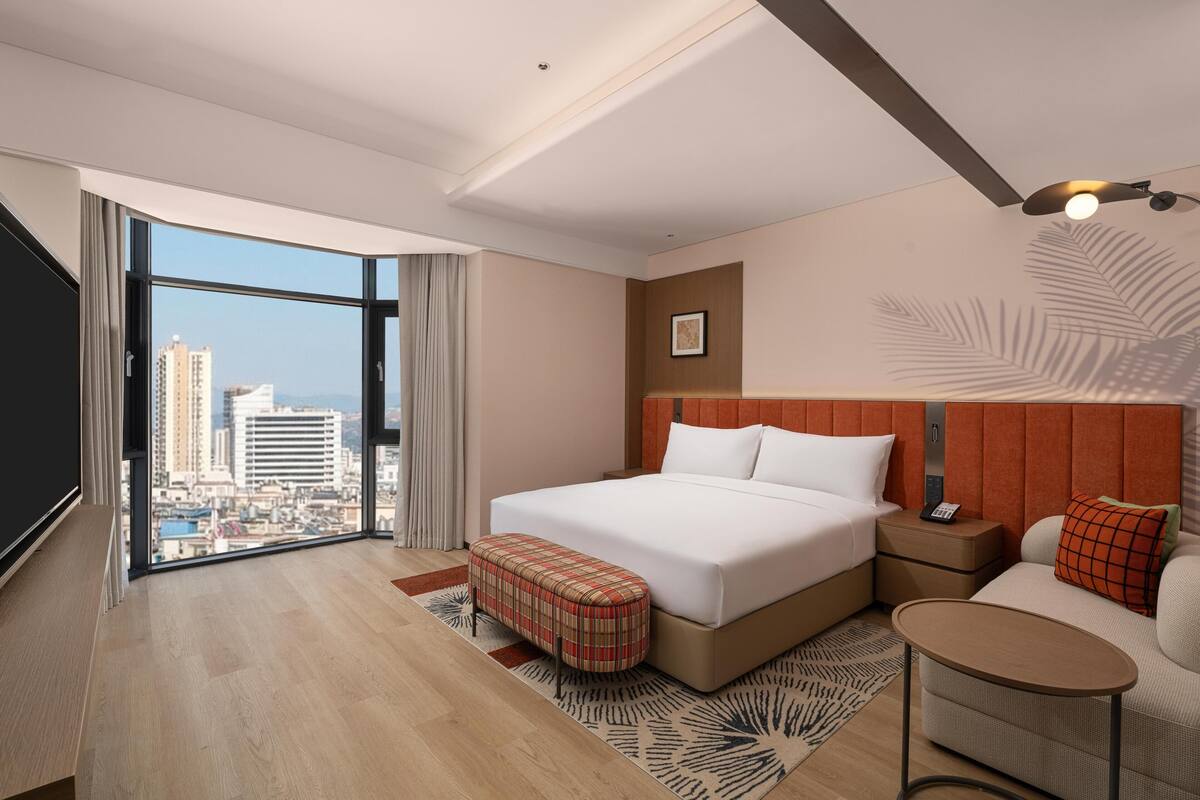 Une chambre d’hôtel moderne avec un grand lit, une petite table, un canapé et une vue sur la ville.