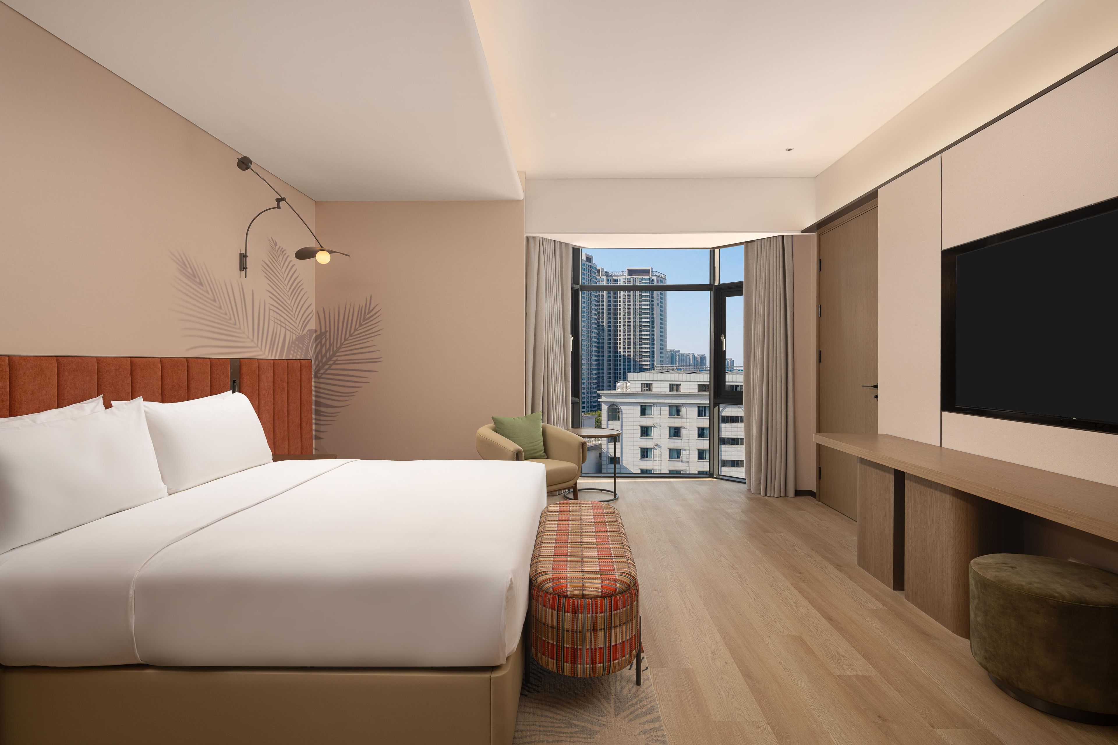 A hotel room with a bed, a TV, a view of the city, and a balcony.