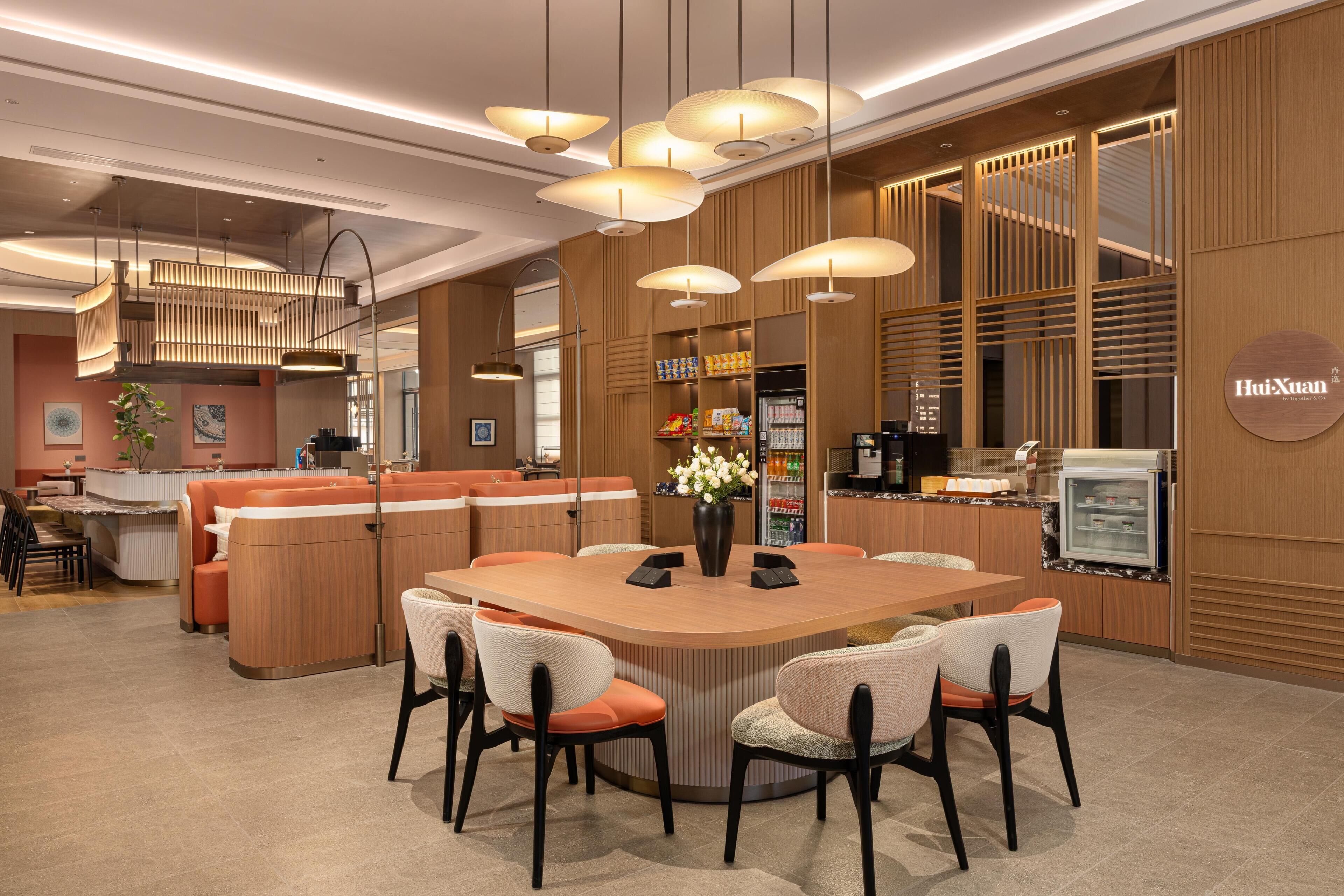 Un moderno vestíbulo de hotel con una mesa redonda central, asientos y una zona de recepción.
