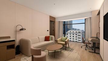 Une chambre d’hôtel moderne équipée d’un canapé, d’un fauteuil, d’une table basse ronde et d’un bureau avec une chaise.