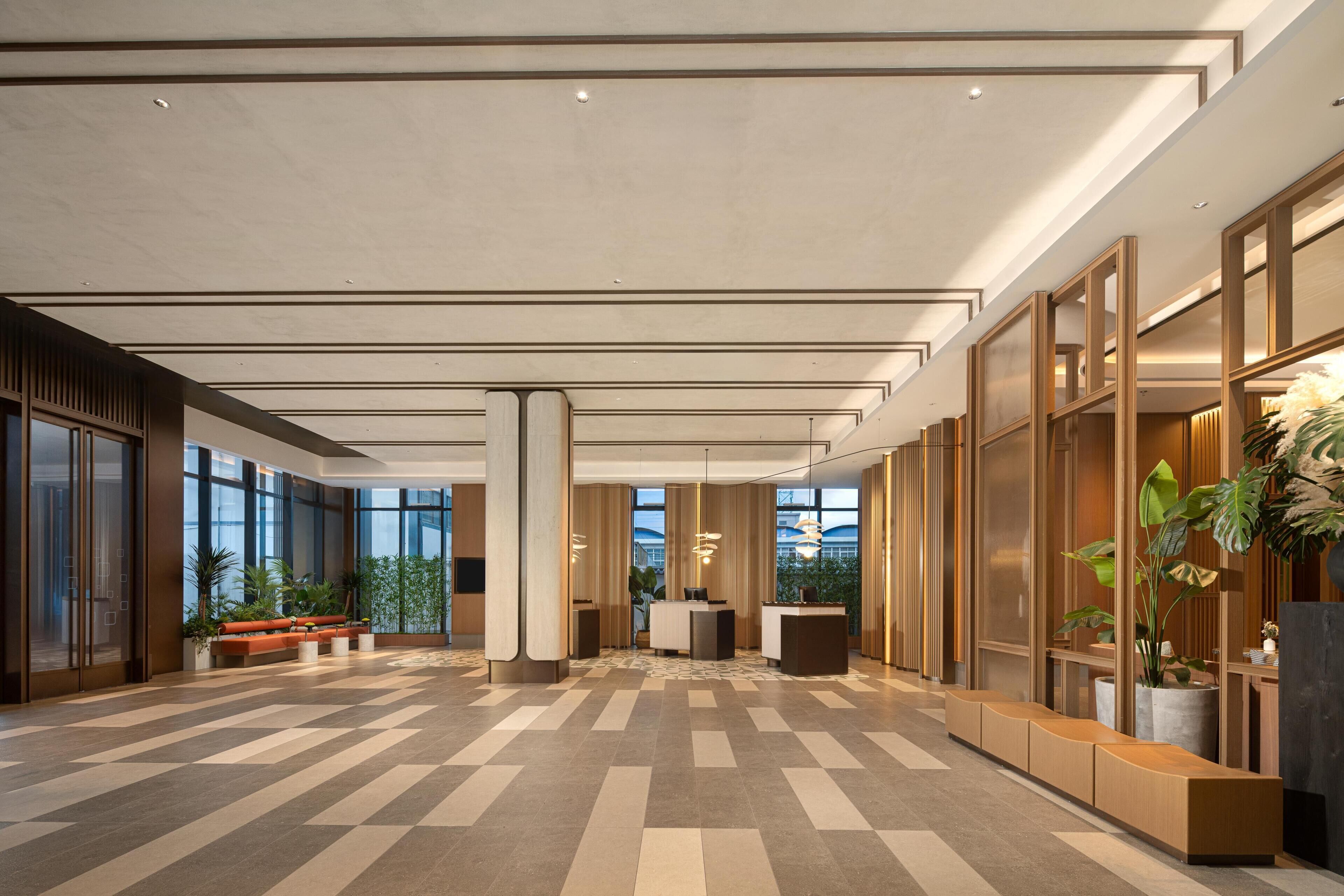 A spacious lobby with a check-in counter, seating areas, and large windows.