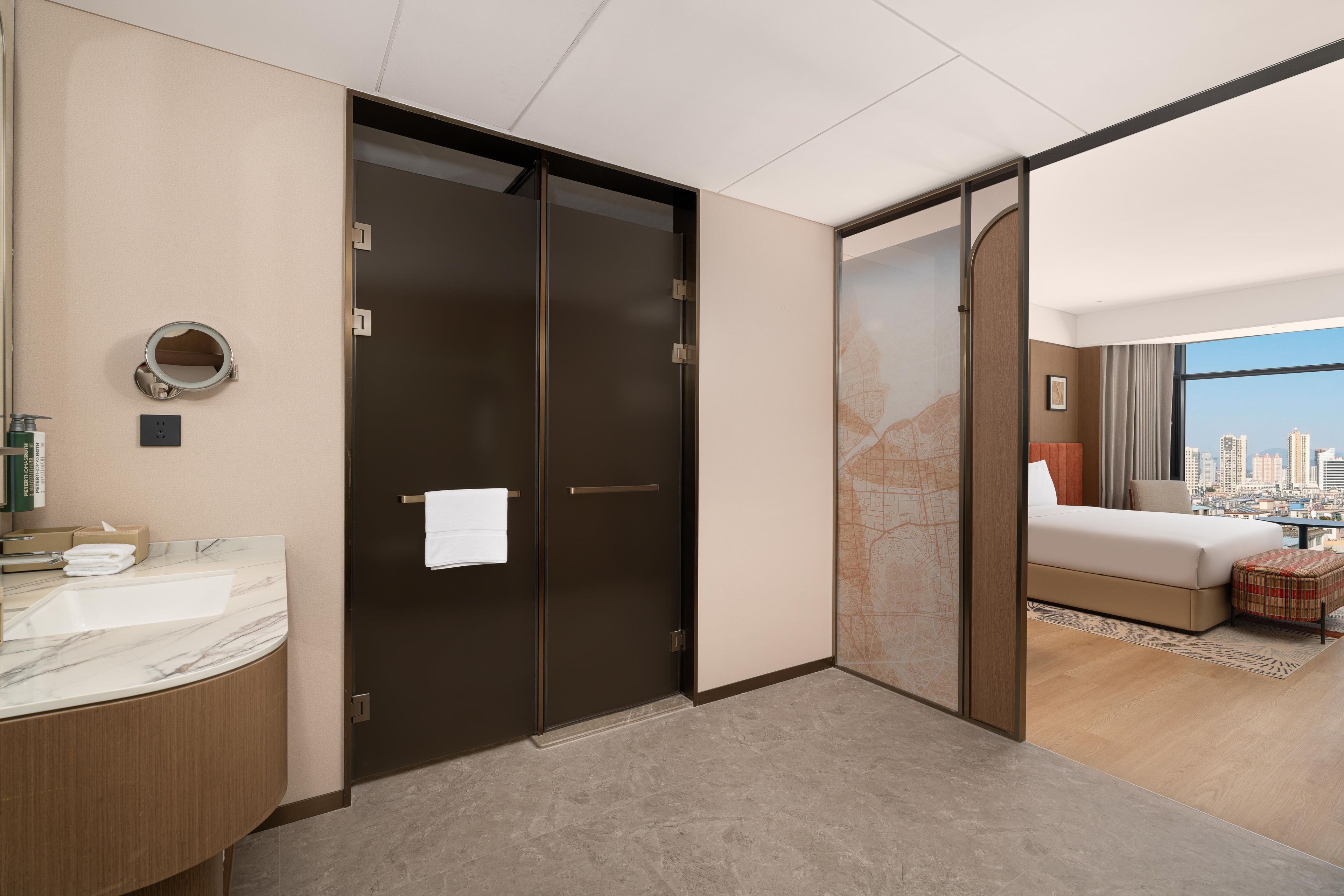 A hotel room with a bathroom, a bed, a city view, and a sliding door.