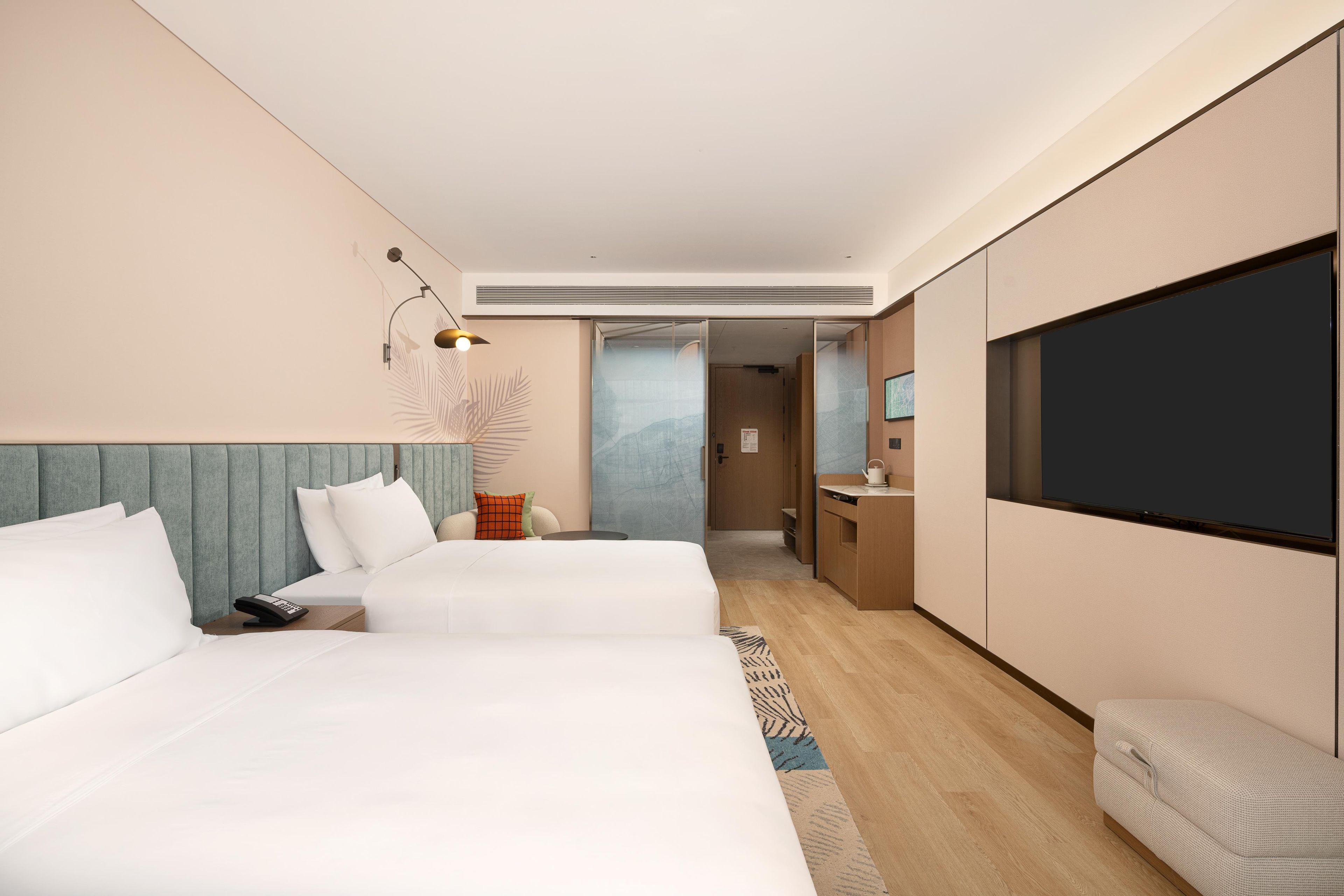 A hotel room with two beds, a desk, a television, and a view of the mountains.