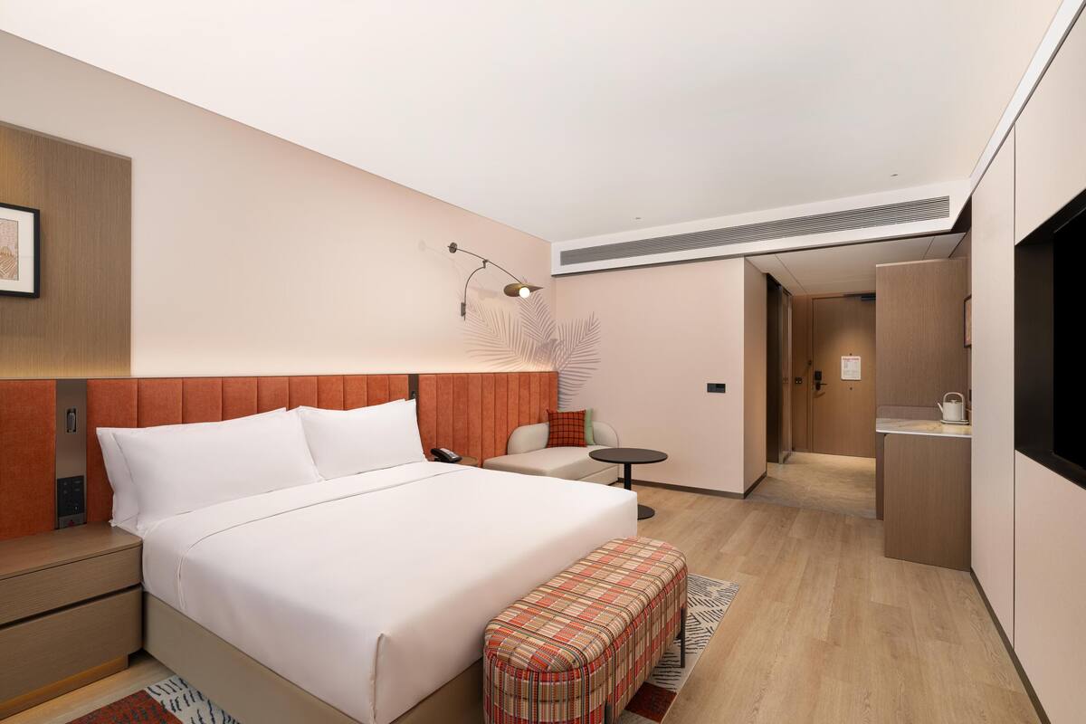 Une chambre d’hôtel comprenant un lit, une petite table, un banc, une kitchenette et une salle de bain.