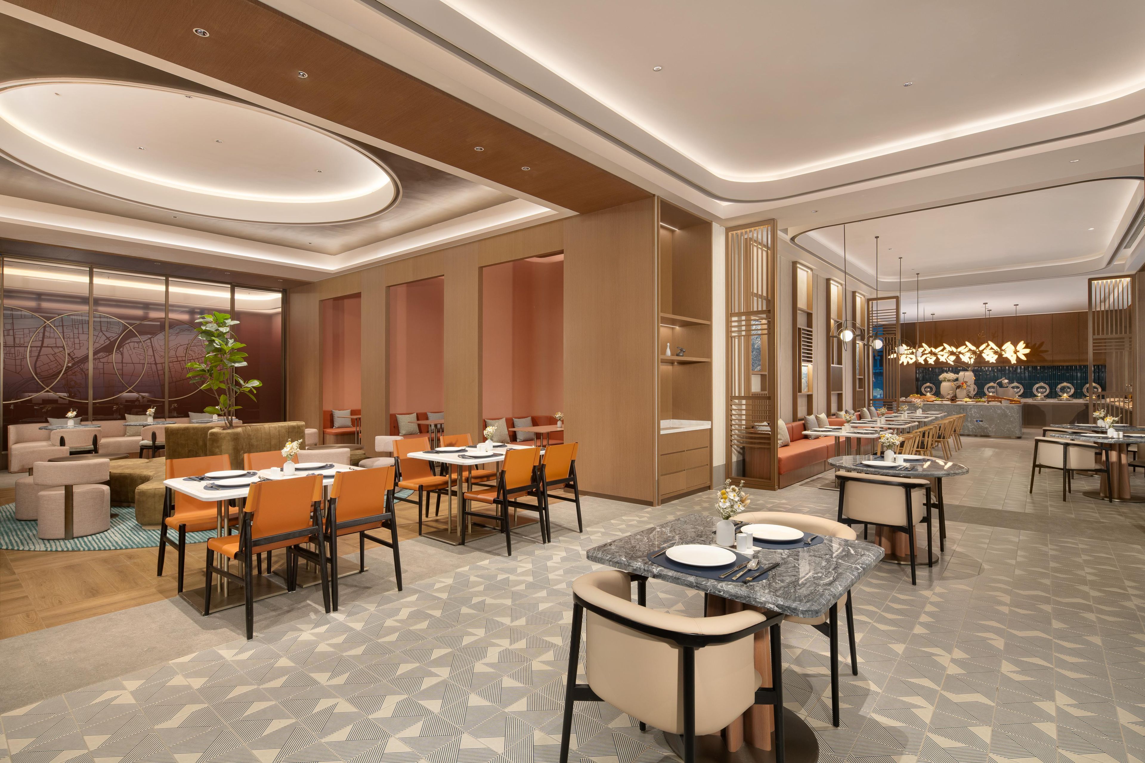 Una hall d'albergo moderna con un'area salotto, un bar e uno spazio dedicato alla ristorazione.