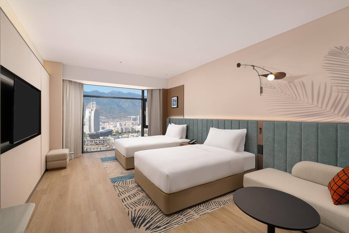 Une chambre d’hôtel avec deux lits, un canapé, une télévision et une vue sur la ville.