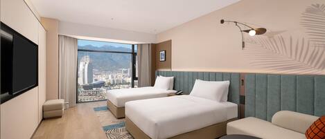 A hotel room with two beds, a sofa, a TV, and a city view.