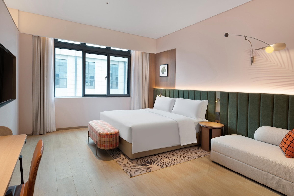 A hotel room with a bed, a sofa, a small table, and a window with curtains.