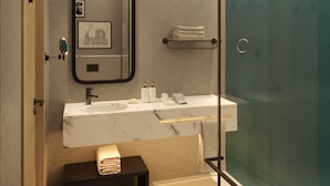 A modern bathroom with a glass shower enclosure, a marble sink, and a small bench with towels. - The 6th Bridge Suites Porto, Tapestry Collection by Hilton (Porto)
