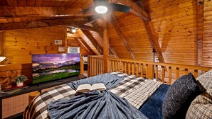 Un dormitorio acogedor tipo cabaña de madera, con cama, televisión y ventilador de techo.