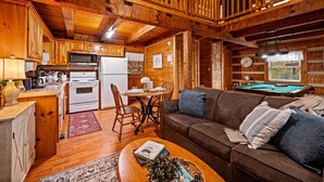 Un acogedor interior de cabaña con paredes de madera, un comedor, una sala de estar con mesa de billar y una cocina con electrodomésticos modernos.