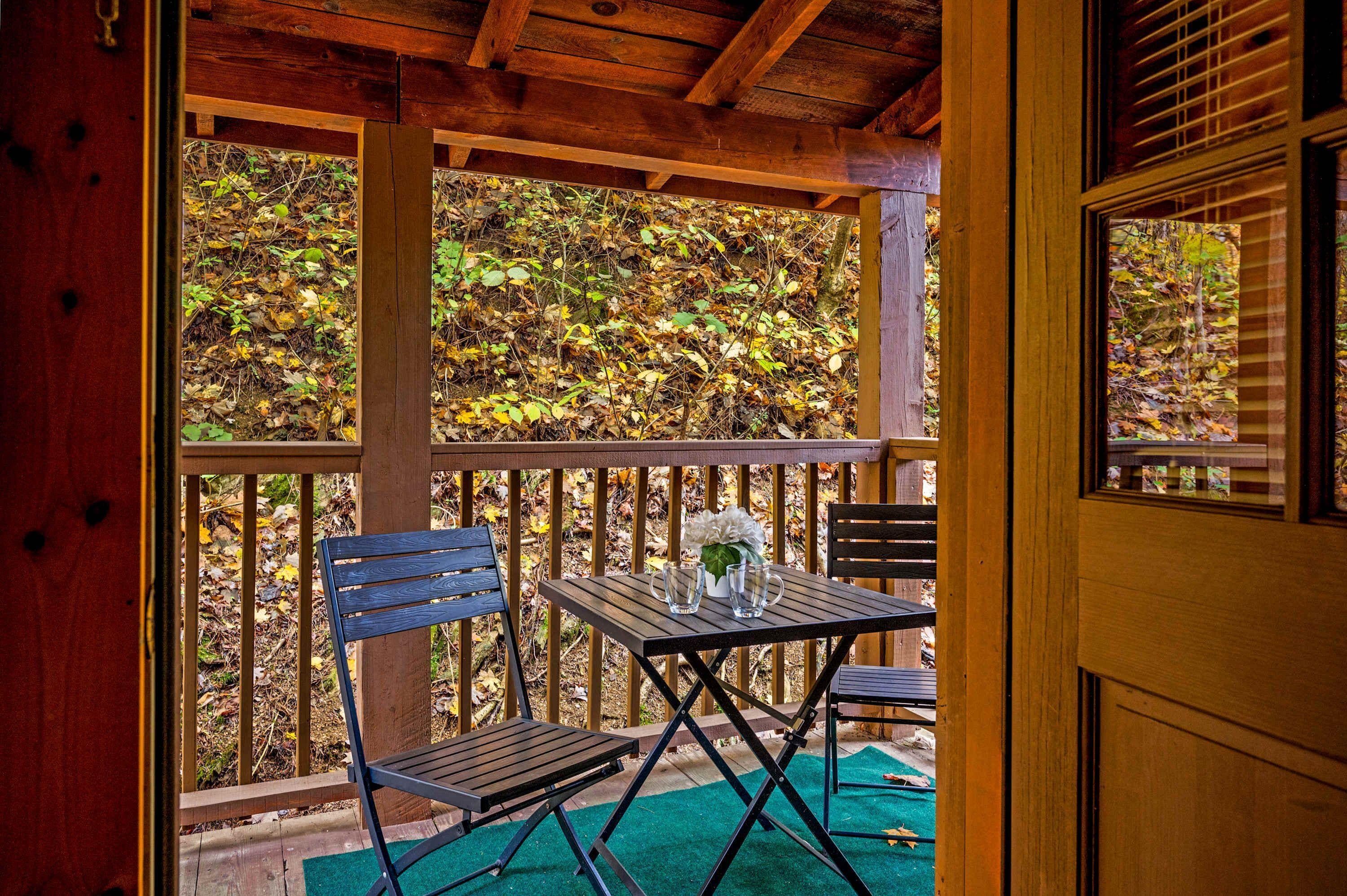 A wooden deck with a table and chairs, overlooking a forested area.