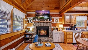 Un interior de cabaña acogedor, con chimenea de piedra, paredes de madera, comedor y cocina.