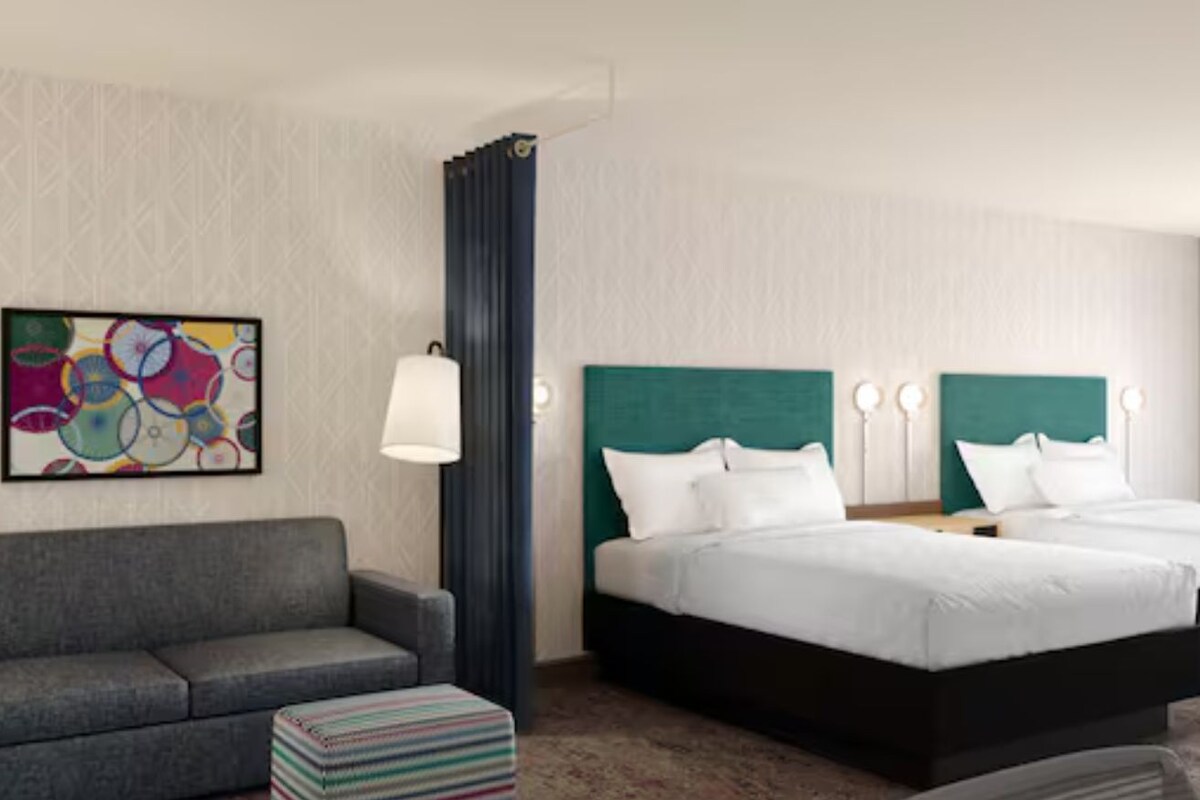 Een hotelkamer met een bank, twee bedden, een kleurrijk abstract schilderij en een behang met patroon.