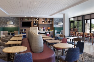 A modern hotel lobby with seating areas, a coffee station, and a large TV screen.