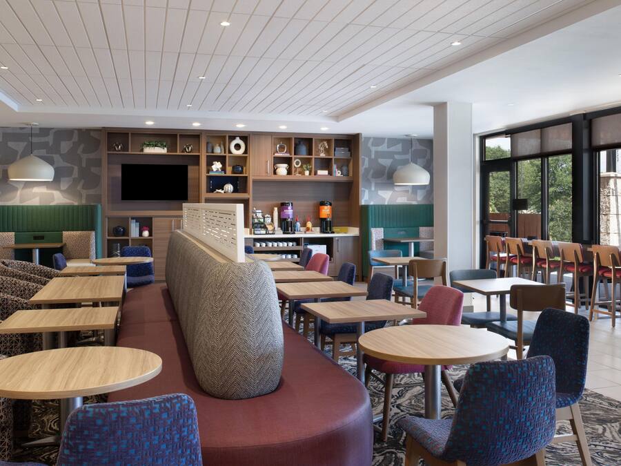 A modern hotel lobby with seating areas, a coffee station, and a large TV screen.