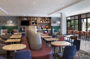 Un moderno vestíbulo de hotel con zonas de estar, una estación de café y una gran pantalla de televisión.