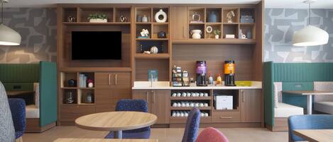 Un interior moderno con televisión de pantalla plana, estanterías de madera con diversos objetos, una estación de café y zonas de estar.