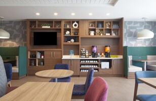Un interior moderno con televisión de pantalla plana, estanterías de madera con diversos objetos, una estación de café y zonas de estar.