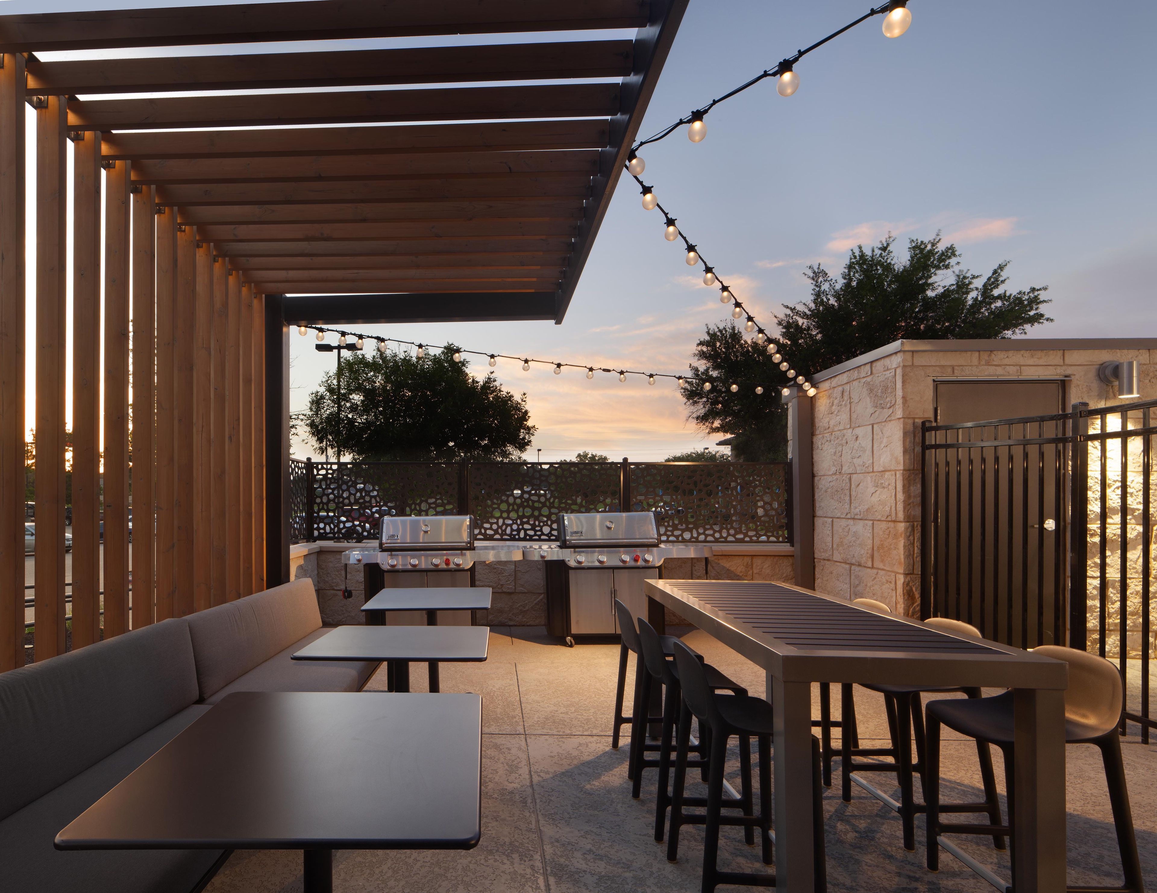 An outdoor patio with a wooden pergola, string lights, a barbecue grill, and seating arrangements.