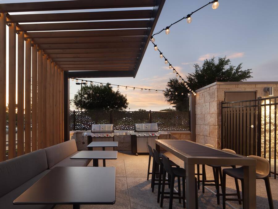 An outdoor patio with a wooden pergola, string lights, a barbecue grill, and seating arrangements.