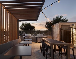 An outdoor patio with a wooden pergola, string lights, a barbecue grill, and seating arrangements. - Home2 Suites by Hilton Texarkana (Texarkana)