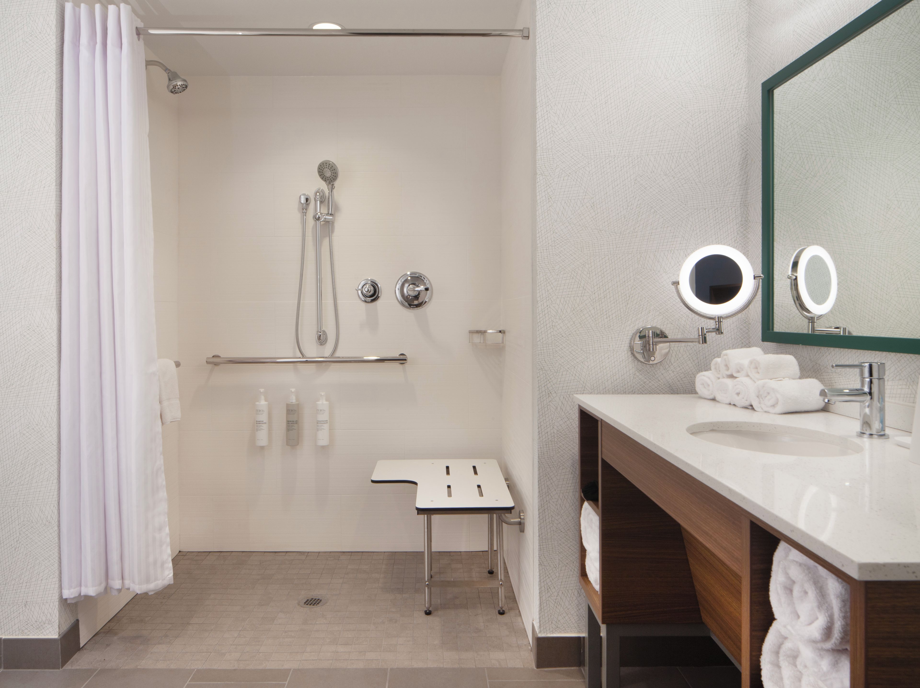 Un baño moderno con ducha, tocador con espejo y un perchero para toallas.