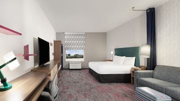 Quarto de hotel com cama, escrivaninha com televisão, sofá, tapete estampado e janela com vista.