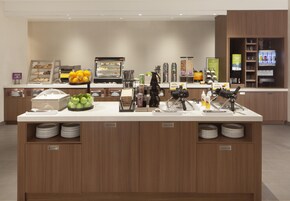 Una estación de desayuno autoservicio con diversas opciones de comida, como gofres, frutas y bebidas.