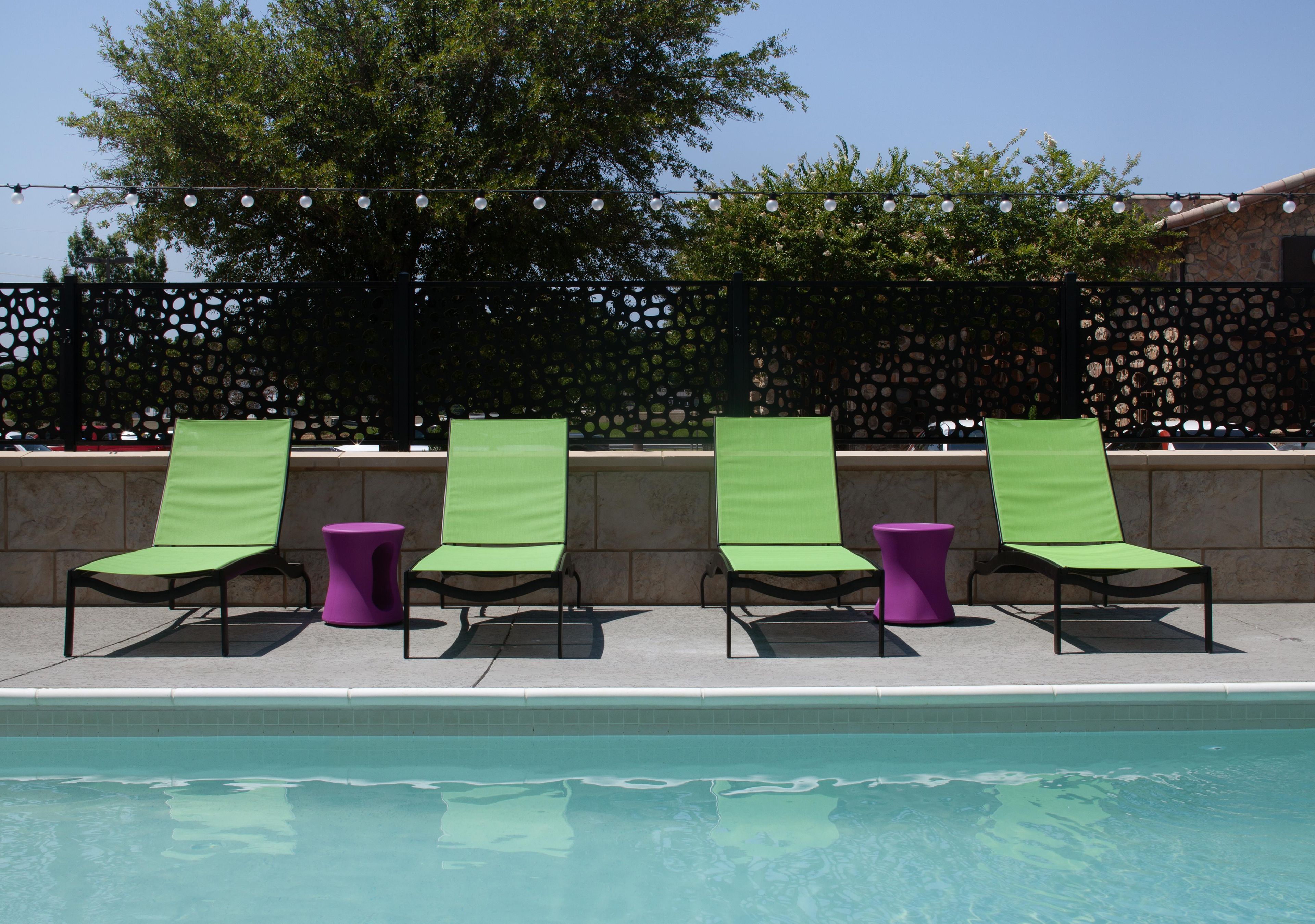 A poolside area with lounge chairs and a small table, a decorative fence, and a clear sky.