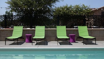 A poolside area with lounge chairs and a small table, a decorative fence, and a clear sky.