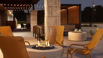 An outdoor seating area with chairs and a round table, a stone pillar, and a fire feature.