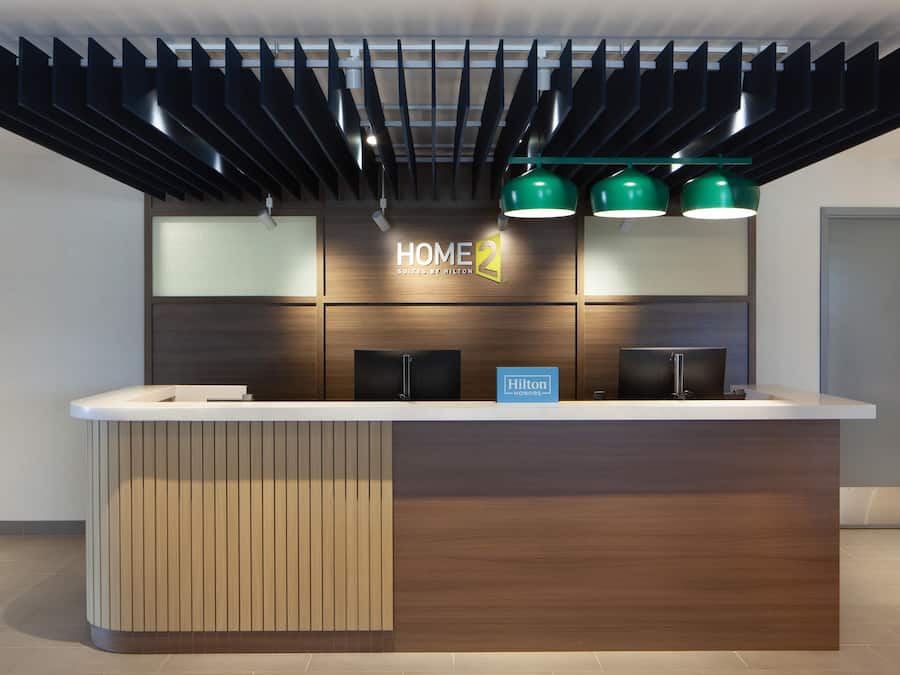 A modern hotel reception desk with a wooden panel design, a digital display, and green pendant lighting.