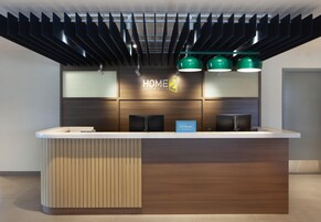 Un moderno mostrador de recepción de hotel con diseño de panel de madera, pantalla digital e iluminación colgante verde.