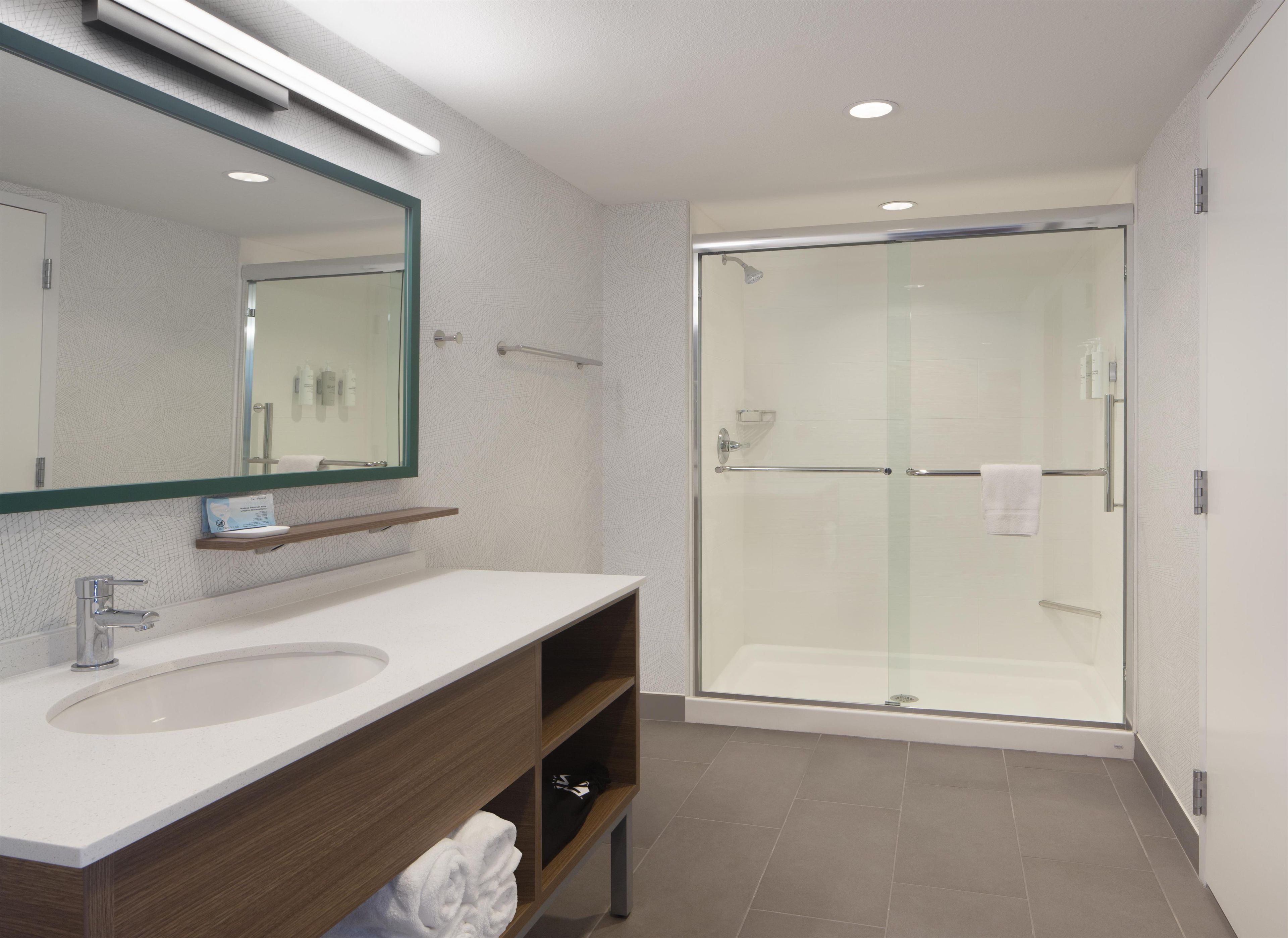 A modern bathroom with a large mirror, a sink, a shower enclosure, and a towel rack.