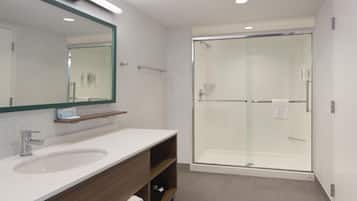 A modern bathroom with a large mirror, a sink, a shower enclosure, and a towel rack.