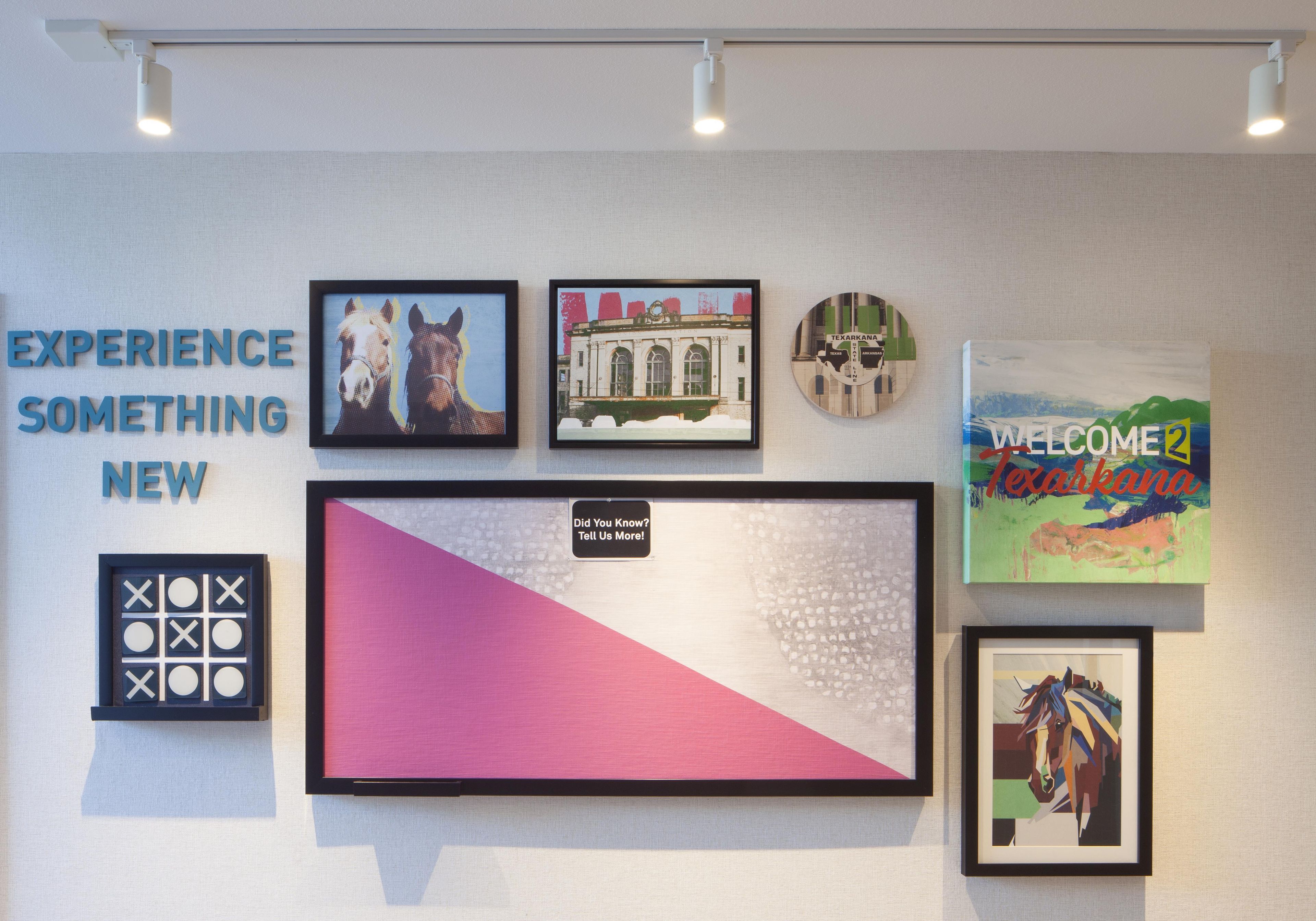 A wall with various framed artworks and a sign that reads 'EXPERIENCE SOMETHING NEW'.