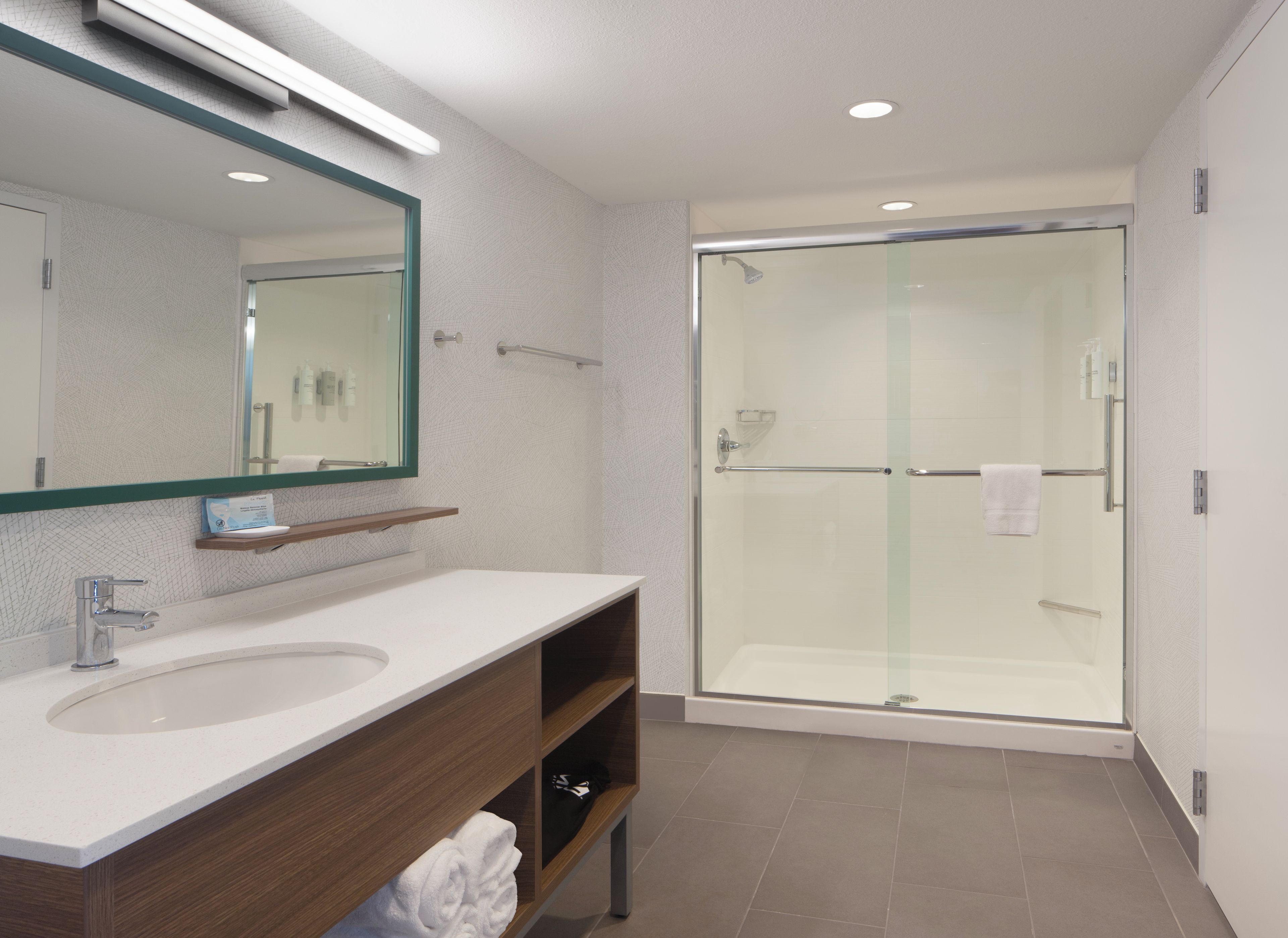A modern bathroom with a large mirror, a sink, a shower enclosure, and a towel rack.