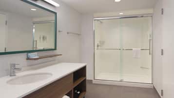 A modern bathroom with a large mirror, a sink, a shower enclosure, and a towel rack.