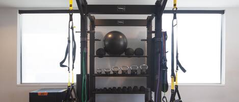Un gimnasio con un entrenador TRX de suspensión, pesas de cañón, balones medicinales y mancuernas.