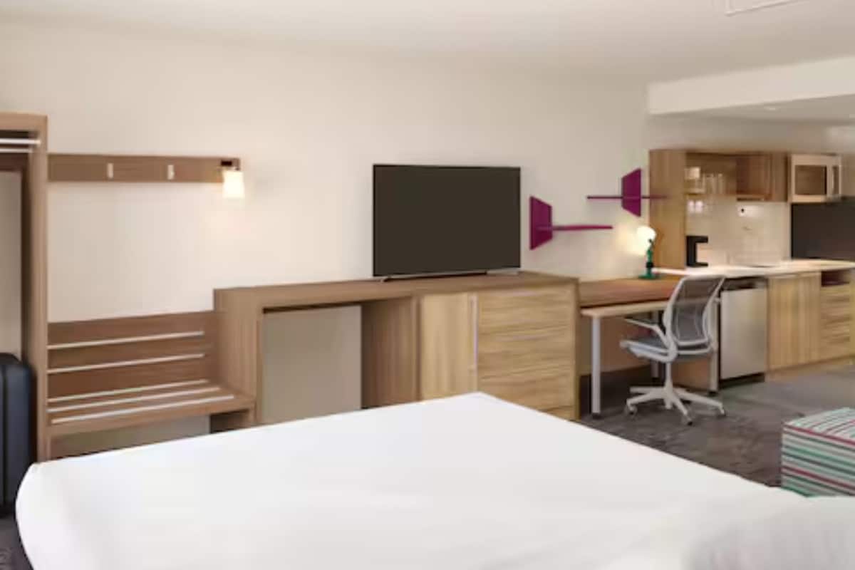 A hotel room with a bed, a desk, a TV, a wardrobe, and a kitchenette.