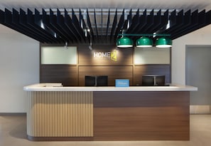 Een modern hotelontvangstbalie met een houten paneelpatroon, een digitaal scherm en groene hanglampen.