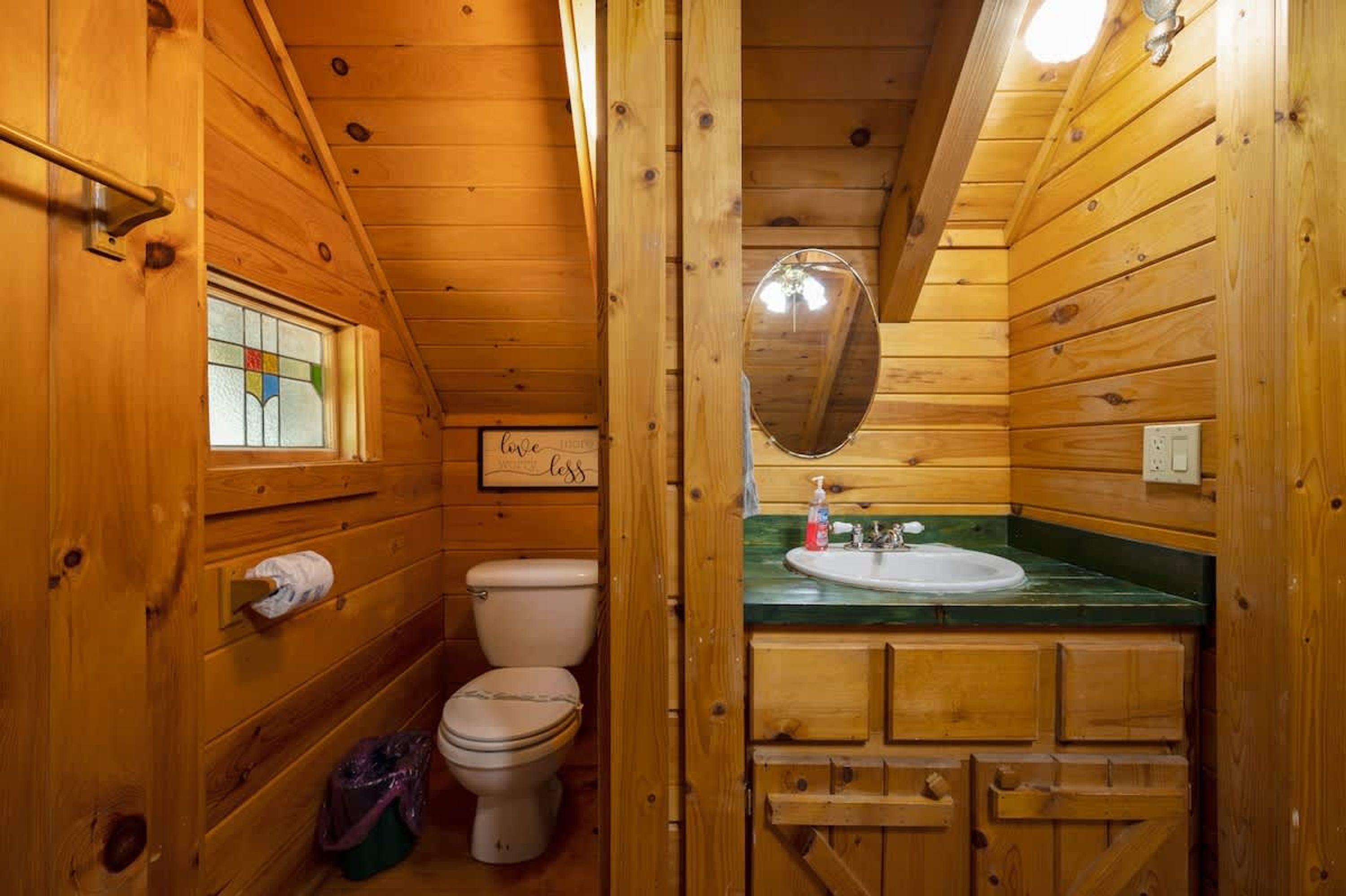 A wooden cabin bathroom with a toilet, sink, and a mirror.