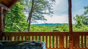 A wooden deck with a hot tub overlooking a forested landscape. - Nice View Log Cabin Fireplace Hot Tub Pool Table (Sevierville)
