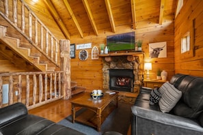 A cozy cabin interior with a fireplace, wooden walls, a staircase, and a leather couch. - Nice View Log Cabin Fireplace Hot Tub Pool Table (Sevierville)