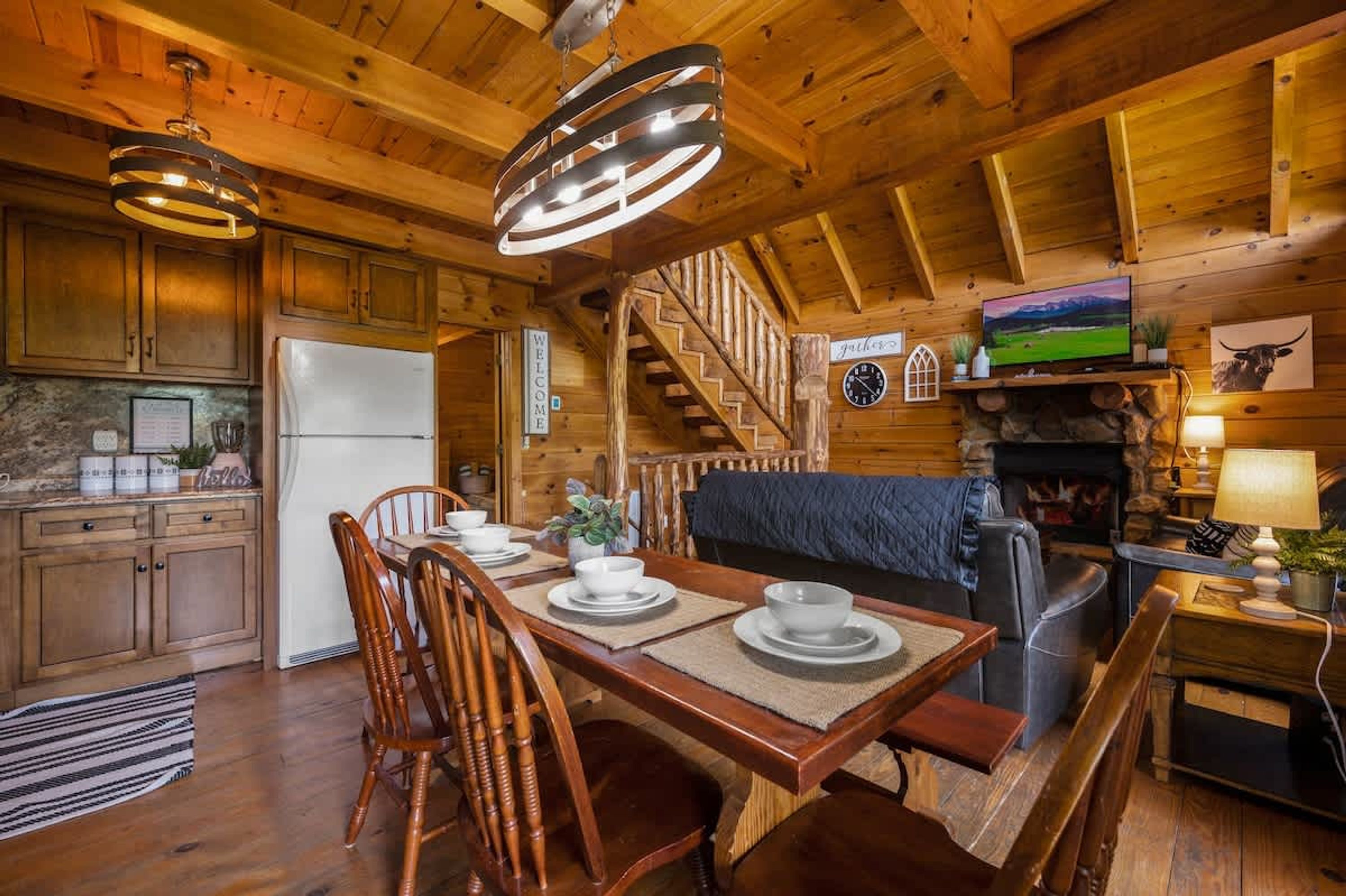 A wooden cabin interior with a dining area, kitchen, and a fireplace.