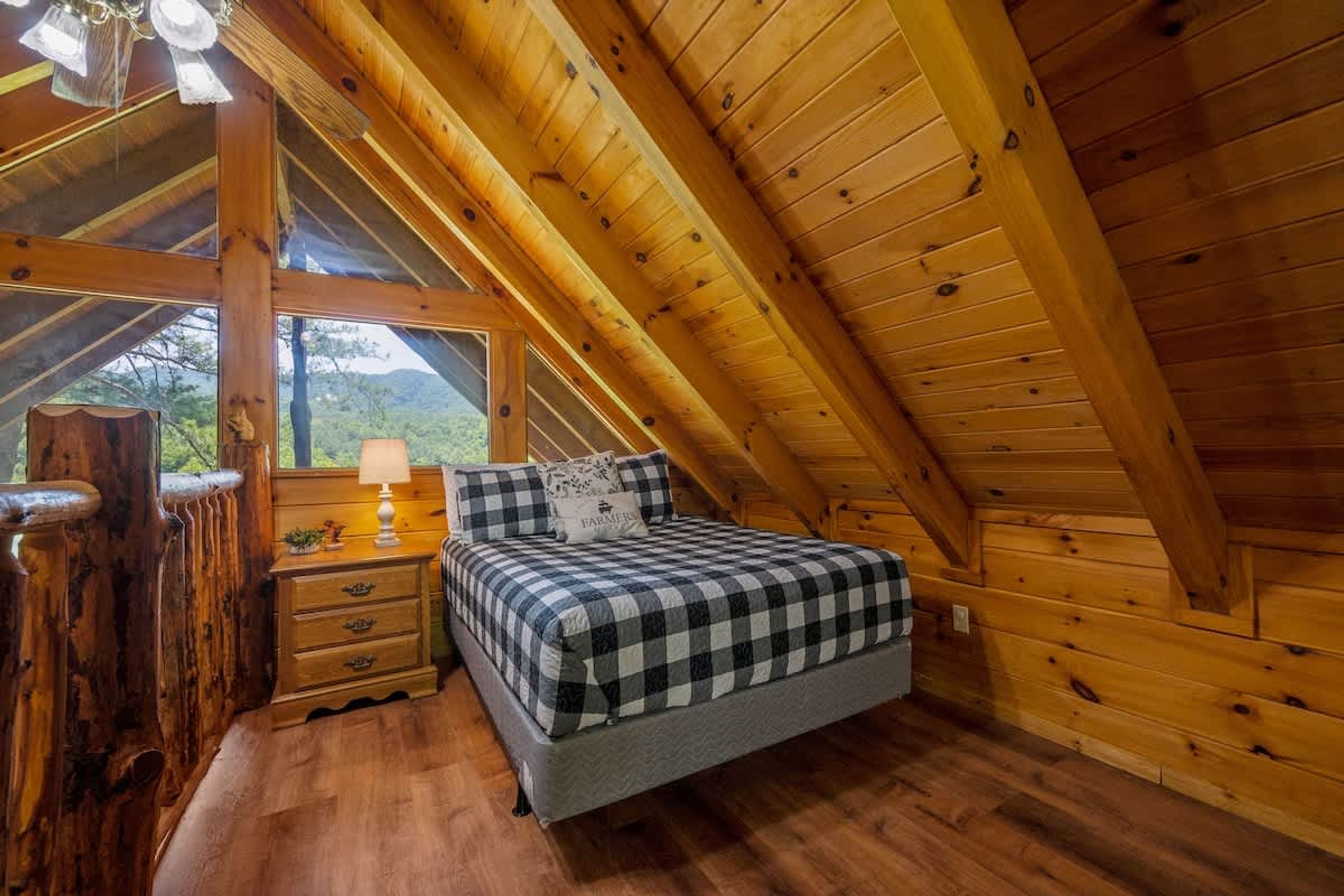 A cozy attic bedroom with a checkered bed, wooden walls, and a nightstand with a lamp.