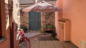 Een terras met een houten tafel, een rode fiets, een groene deur en bloempotten.