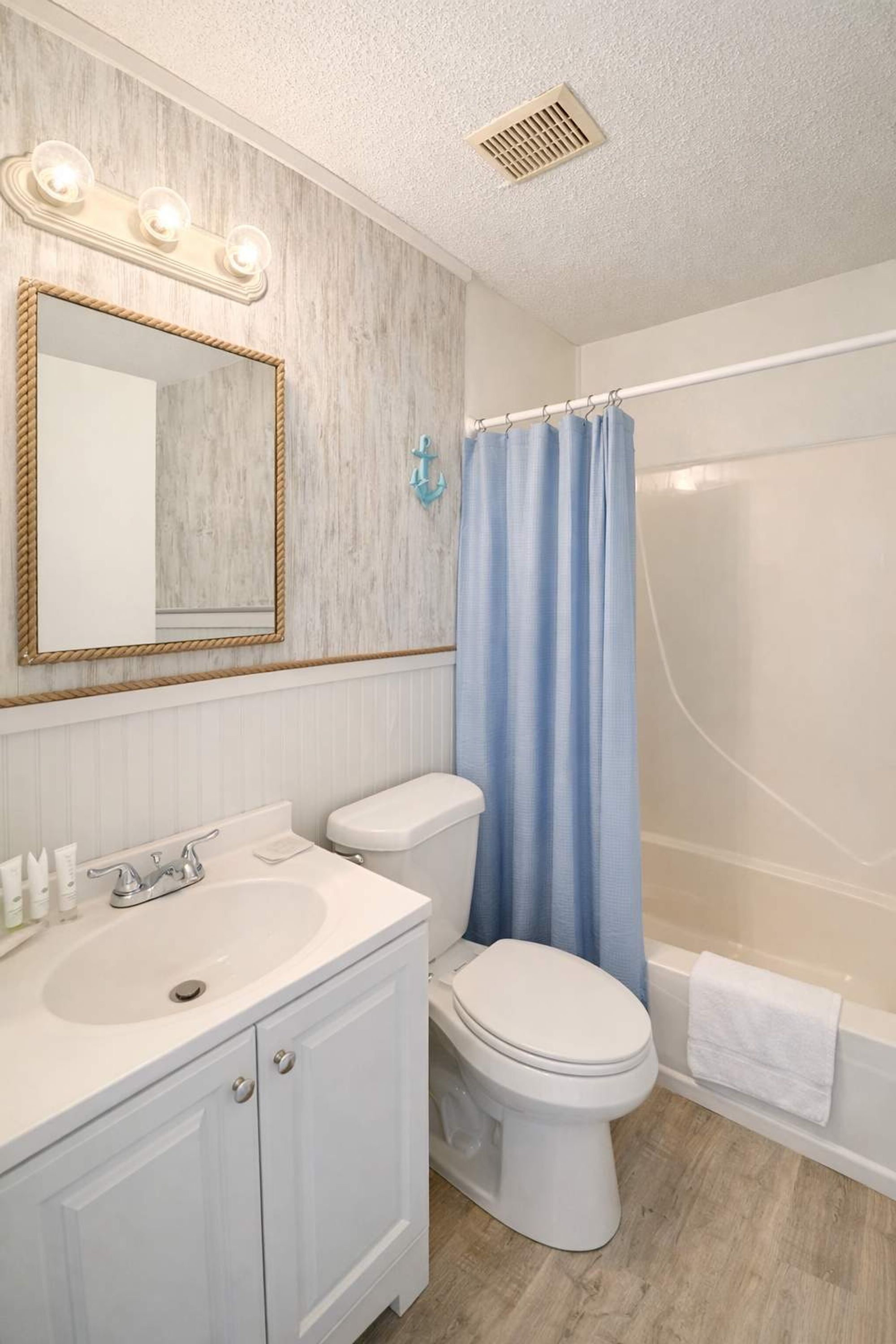 Une salle de bain avec un lavabo blanc, des toilettes, une douche avec un rideau bleu et un miroir avec des lumières.